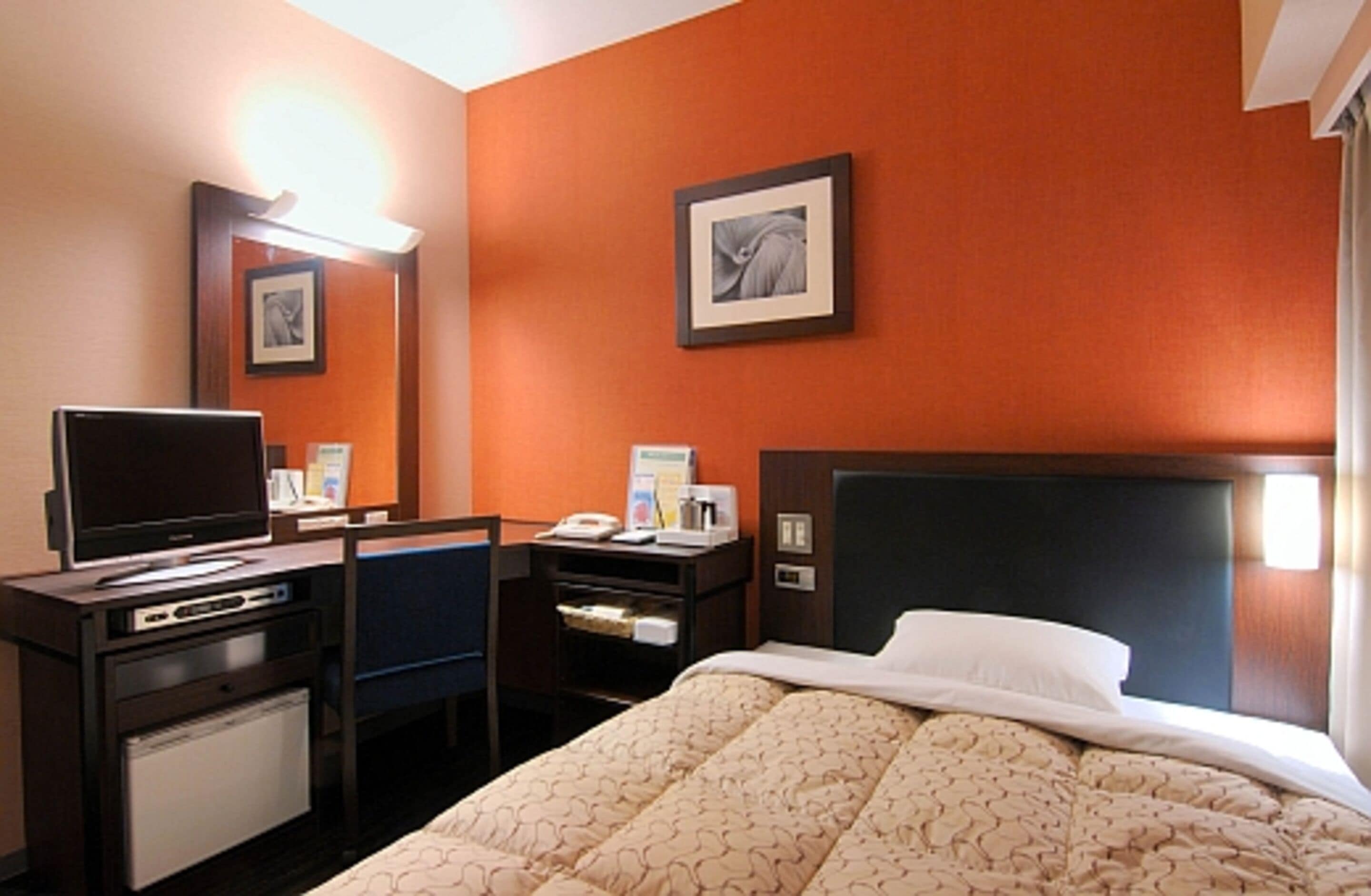 A hotel room with a bed, a desk with a computer, a television, and a small refrigerator.