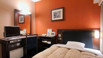 A hotel room with a bed, a desk with a computer, a television, and a small refrigerator.