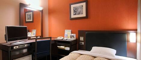 A hotel room with a bed, a desk with a computer, a television, and a small refrigerator.