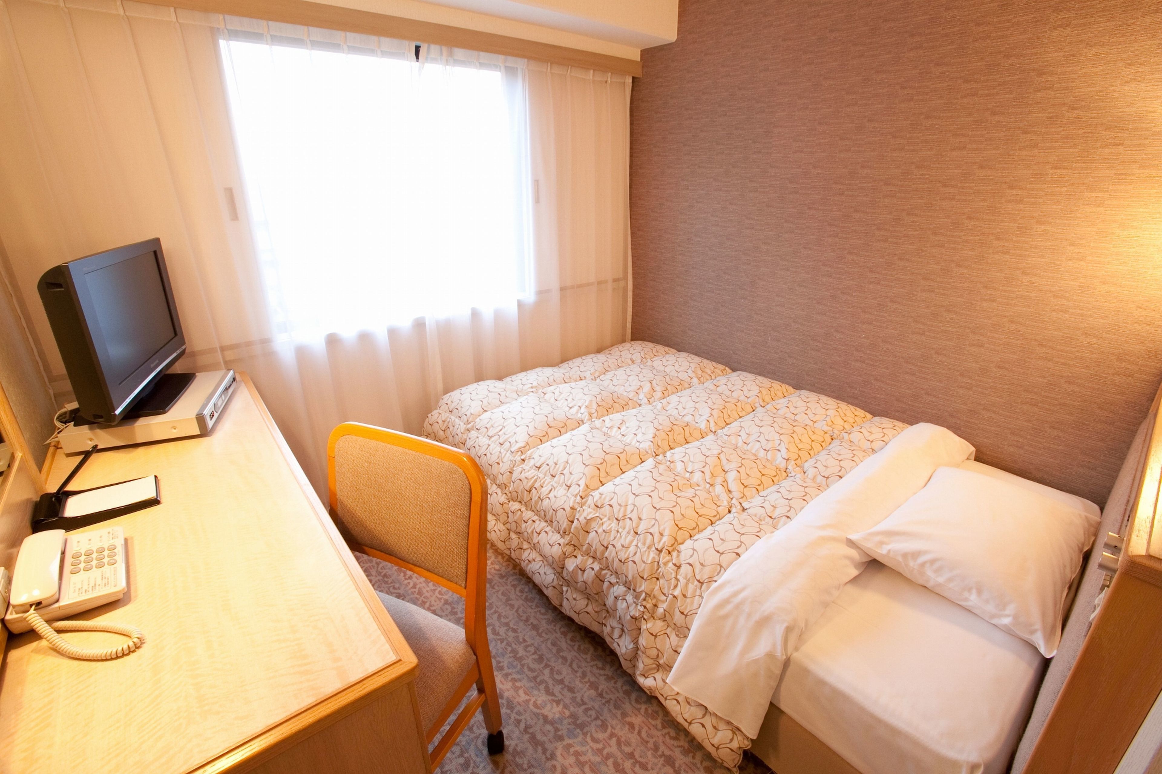 Una camera d'albergo con un letto, una scrivania con computer e telefono, e una finestra con tende.