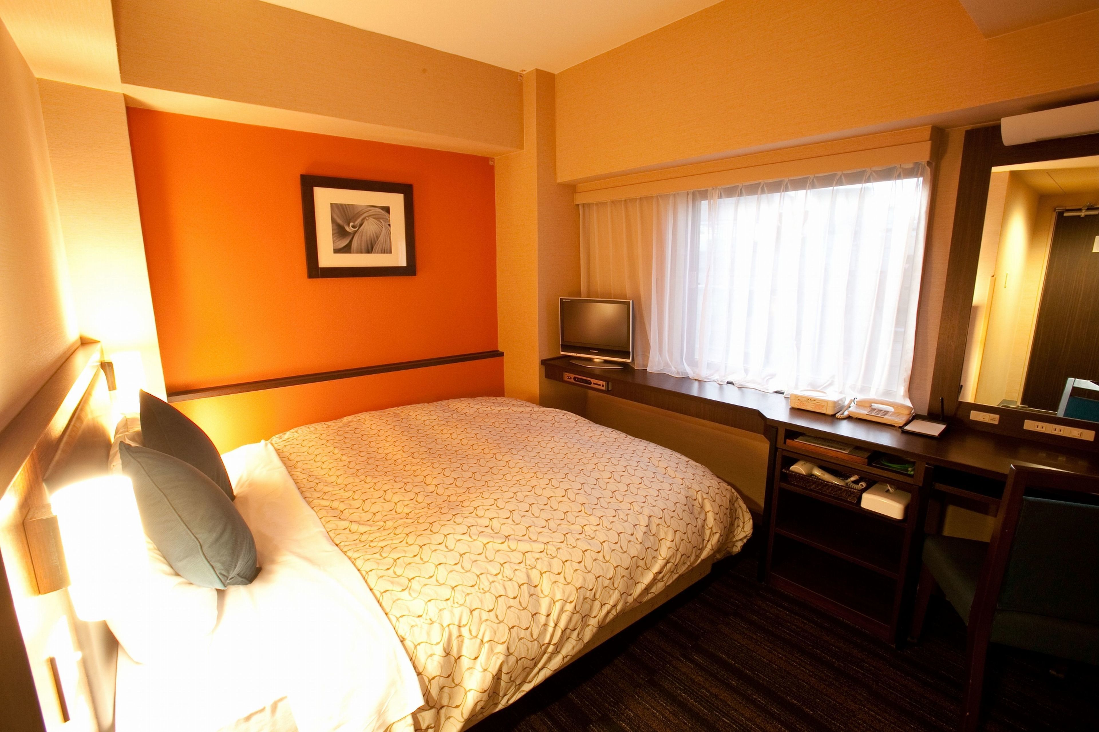 A hotel room with a bed, a desk, a television, and a window with curtains.