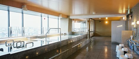 A modern indoor pool area with a glass barrier, steps leading to the pool, and a row of sinks with soap dispensers.