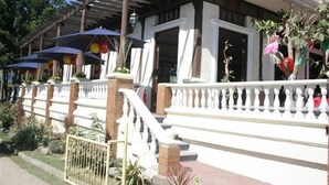A covered outdoor area with umbrellas, a white railing, and plants. - Rio Grande de Laoag Resort Hotel (Laoag)