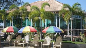 A poolside area with lounge chairs and umbrellas, a building with a tiled roof, and palm trees. - Rio Grande de Laoag Resort Hotel (Laoag)