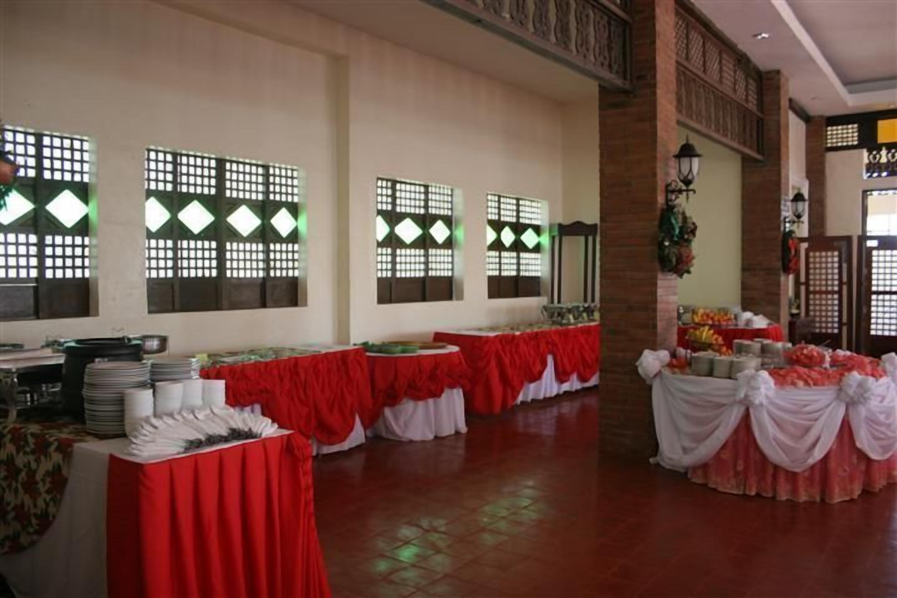 Un salón de banquetes con mesas dispuestas para una recepción, con techo alto y celosías decorativas en las ventanas.
