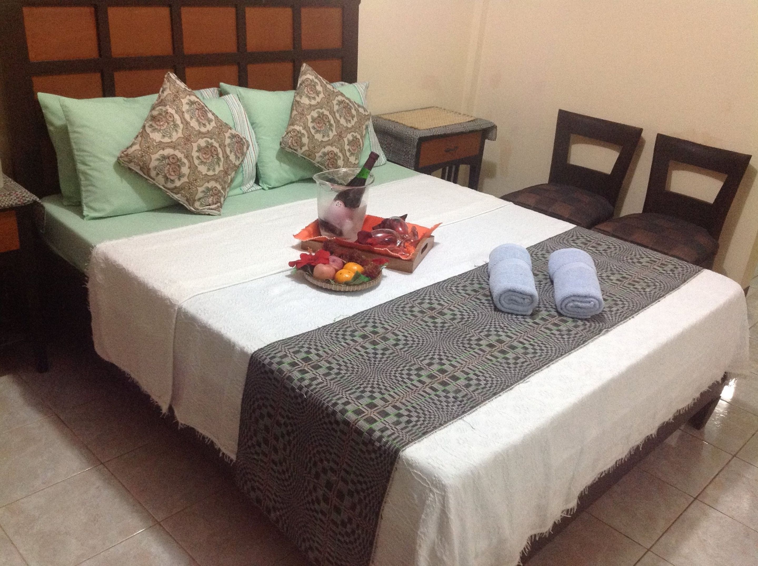 Una cama bien hecha con una colcha estampada, almohadas y toallas enrolladas.