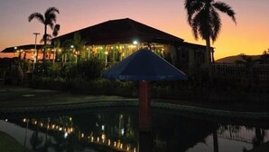 A building with a reflective pool at dusk, palm trees, and a clear sky. - Rio Grande de Laoag Resort Hotel (Laoag)