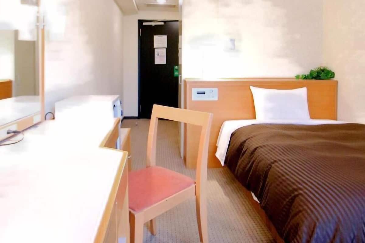 A hotel room with a bed, a desk, a chair, and a door.