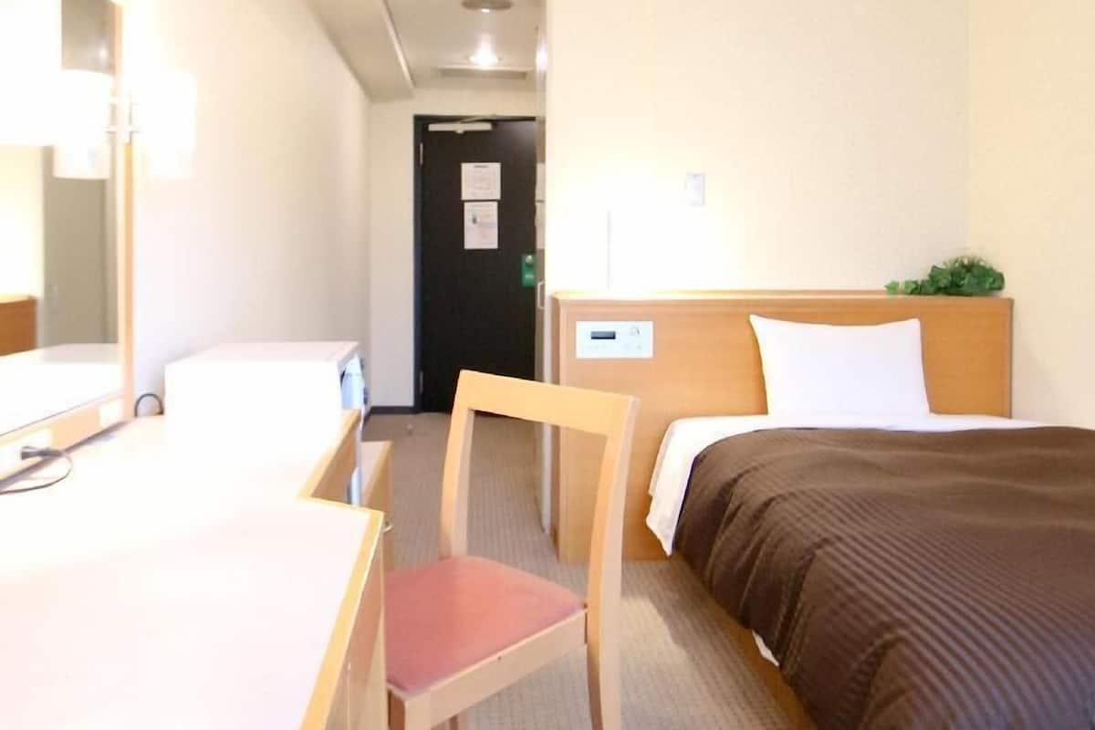 A hotel room with a bed, a desk, a chair, a mirror, and a door.