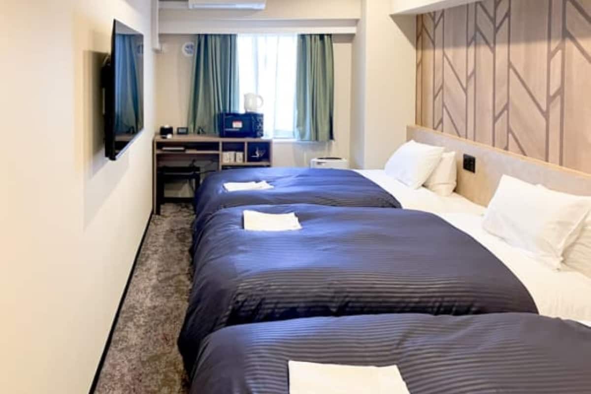 A hotel room with two beds, a desk, a chair, a TV, and a window with curtains.