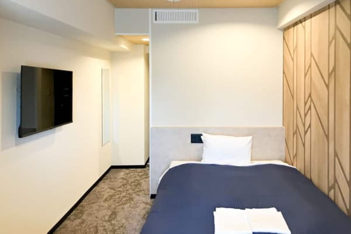 A hotel room with a bed, a flat-screen TV mounted on the wall, and a patterned headboard.