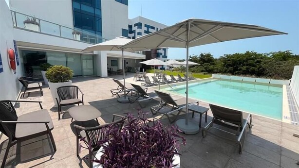 A rooftop pool area with lounge chairs and umbrellas, a modern building with large windows, and a clear view of the sky. - Hampton Inn by Hilton Ciudad del Carmen Campeche (Ciudad del Carmen)