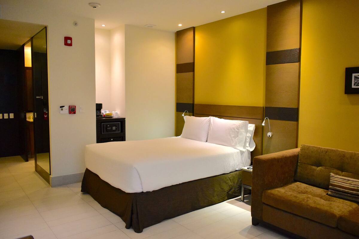 Una habitación de hotel con una cama grande, un sofá, una mesita de noche y un espejo.