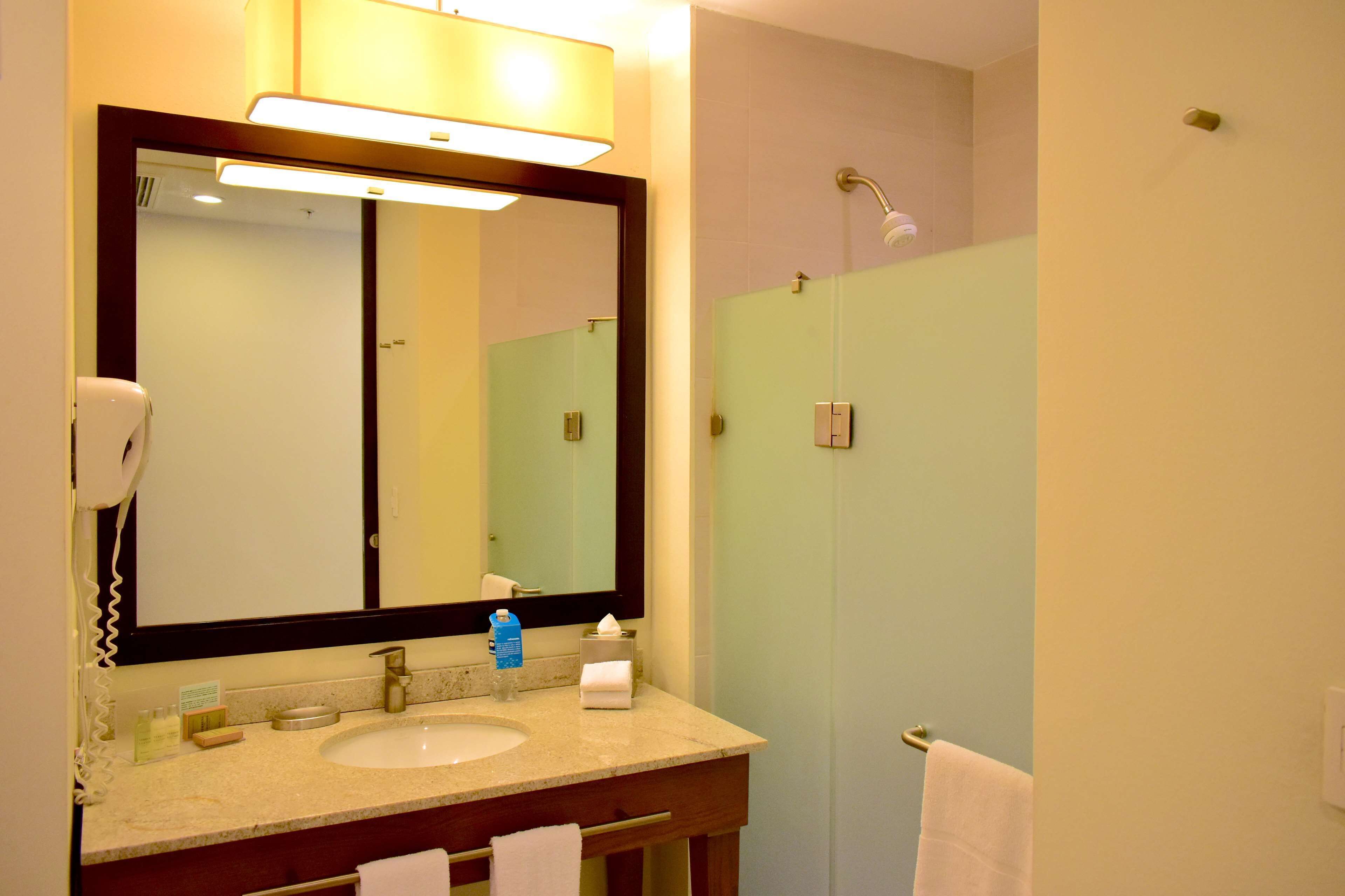 A bathroom with a large mirror, a sink, a towel rack, and a shower area.