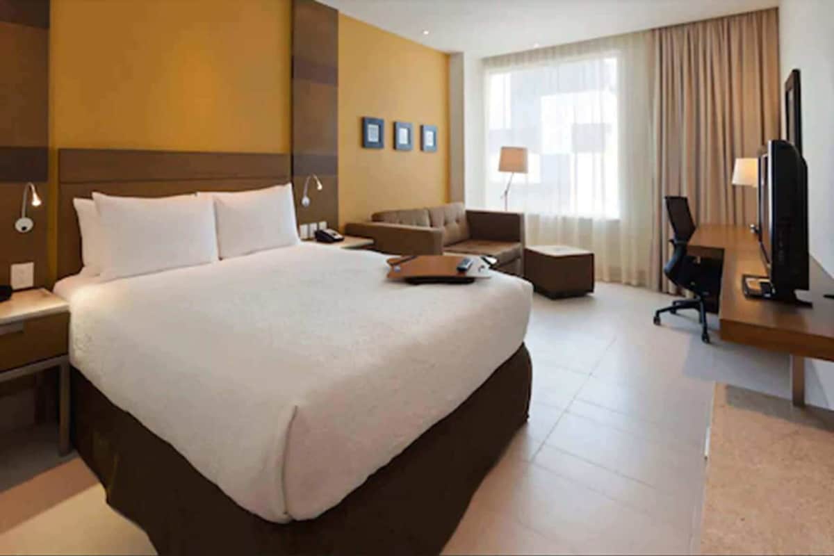 Una habitación de hotel con una cama grande, un escritorio con computadora, una silla, un sofá y un televisor.