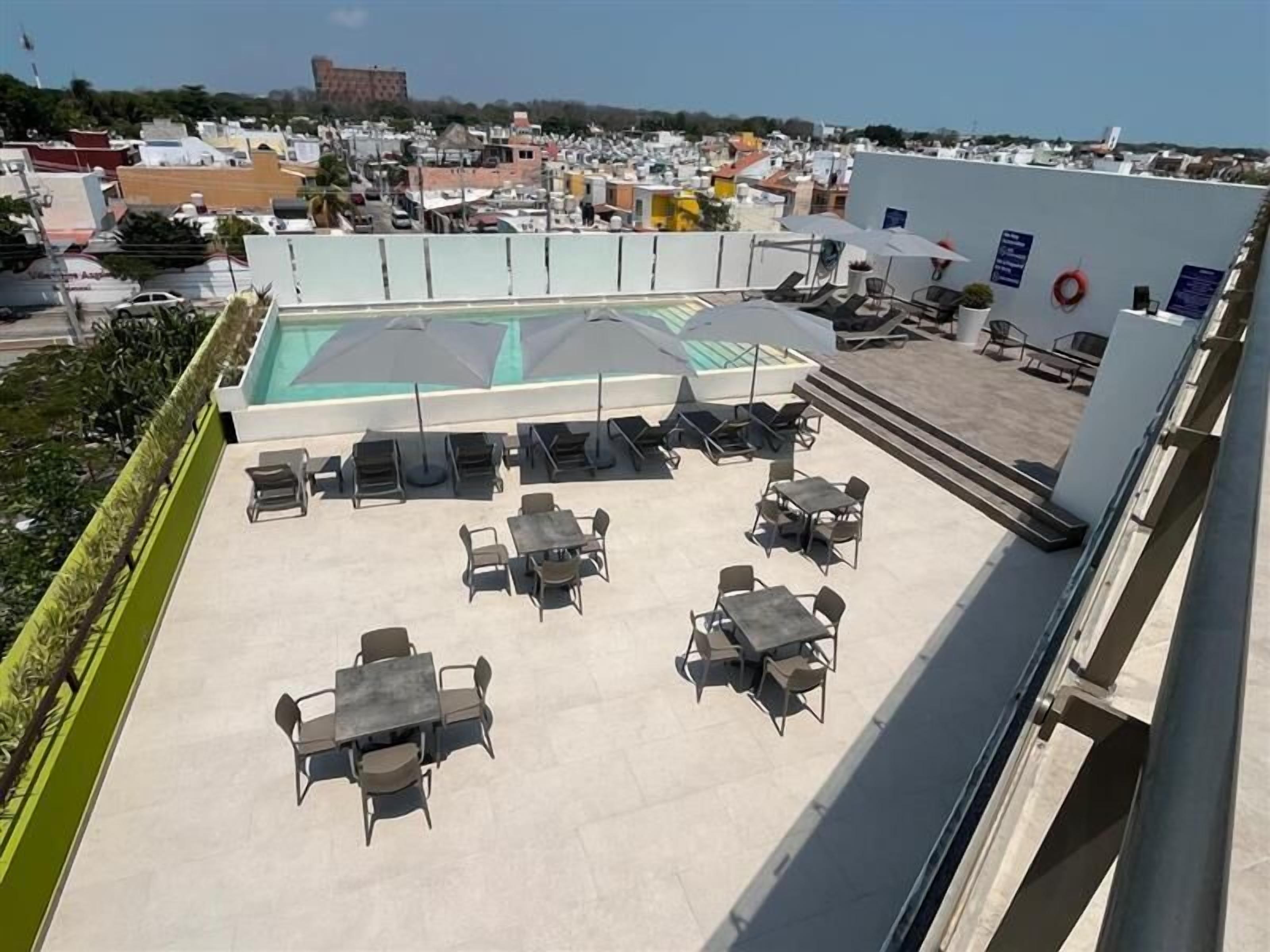 A rooftop terrace with a pool, lounge chairs, and tables.