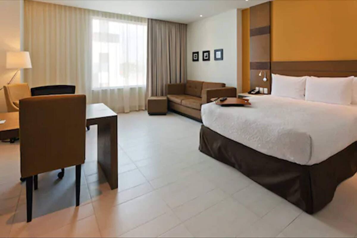 Una habitación de hotel con cama, escritorio, silla, sofá y ventana con cortinas.
