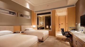 Une chambre d’hôtel avec deux lits, un bureau, une chaise, une télévision et une salle de bain visible à travers une porte ouverte.