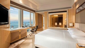 A hotel room with a large bed, a desk with a chair, a television, and a view of the ocean. - Hilton Dalian (Dalian)