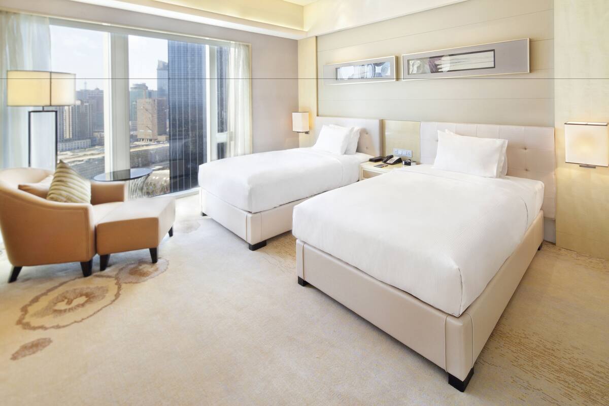 Habitación de hotel con dos camas, un sofá, una mesita de noche y vistas a la ciudad.