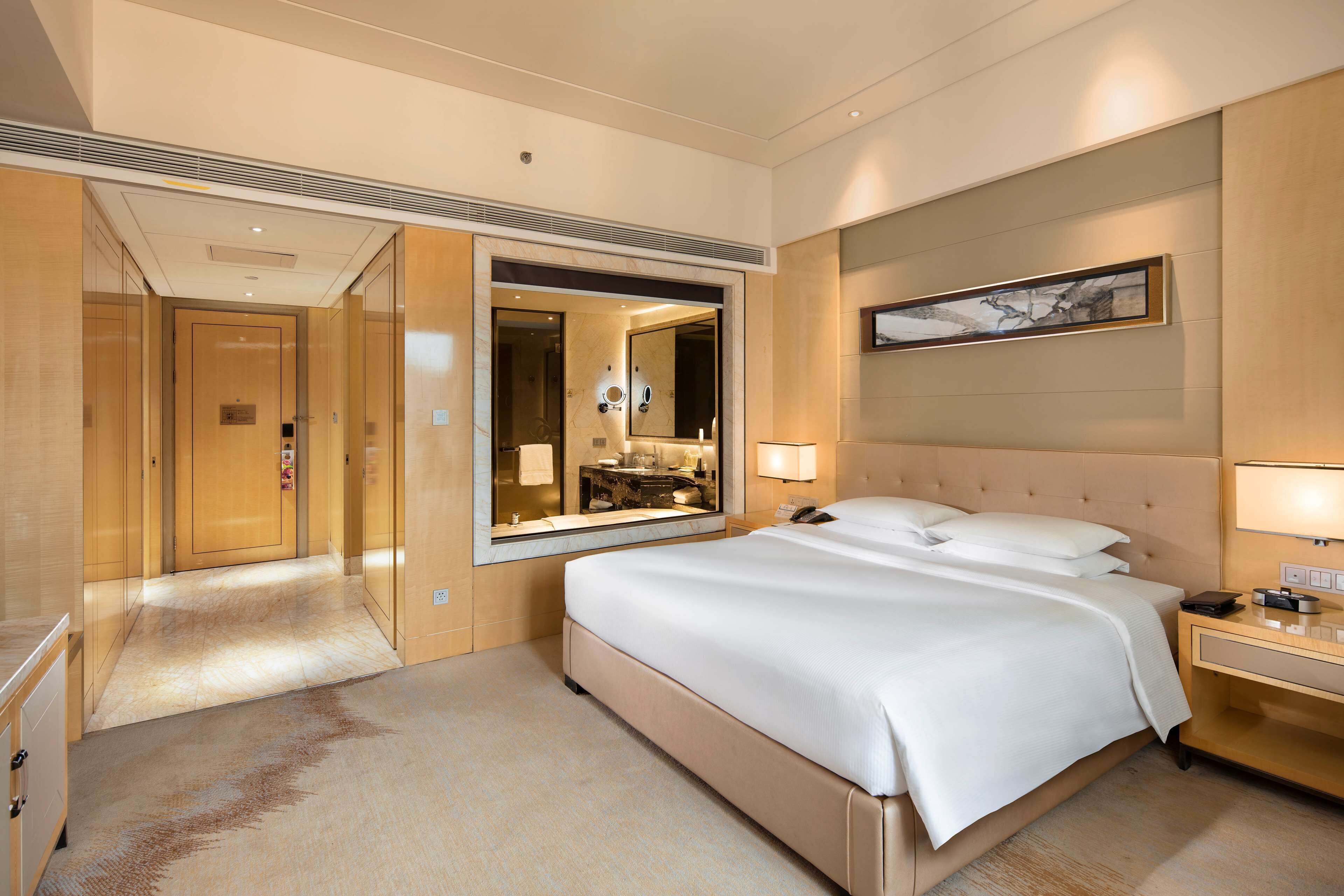 Una camera d'albergo con un letto grande, un comodino con una lampada, uno specchio e un quadro appeso al muro.
