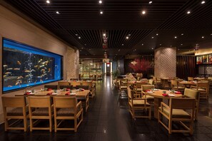 A restaurant with wooden tables and chairs, a large aquarium on the wall, and a brick wall with a glass window. - Hilton Dalian (Dalian)