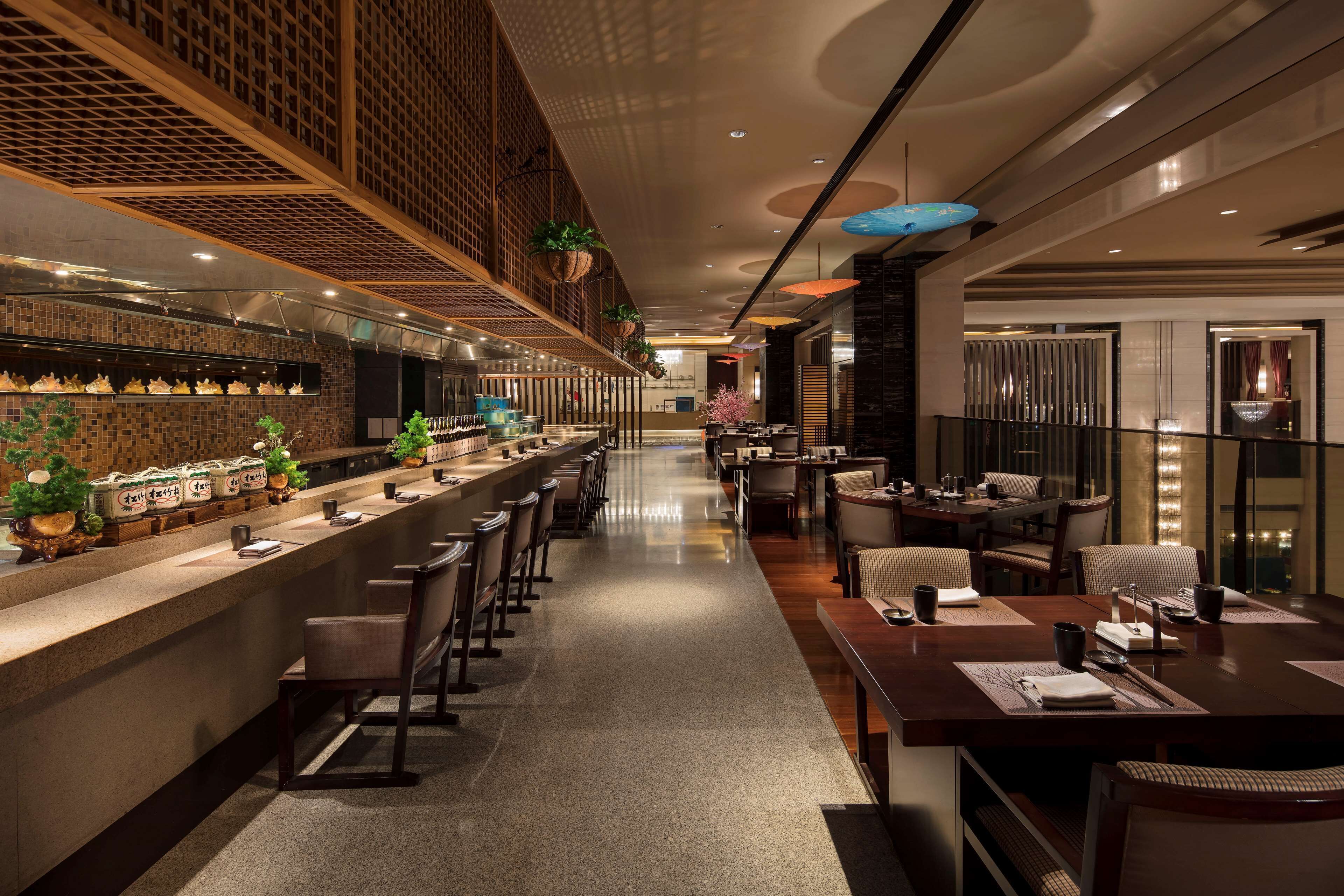 A modern restaurant with a long counter, bar seating, and a dining area with tables and chairs.