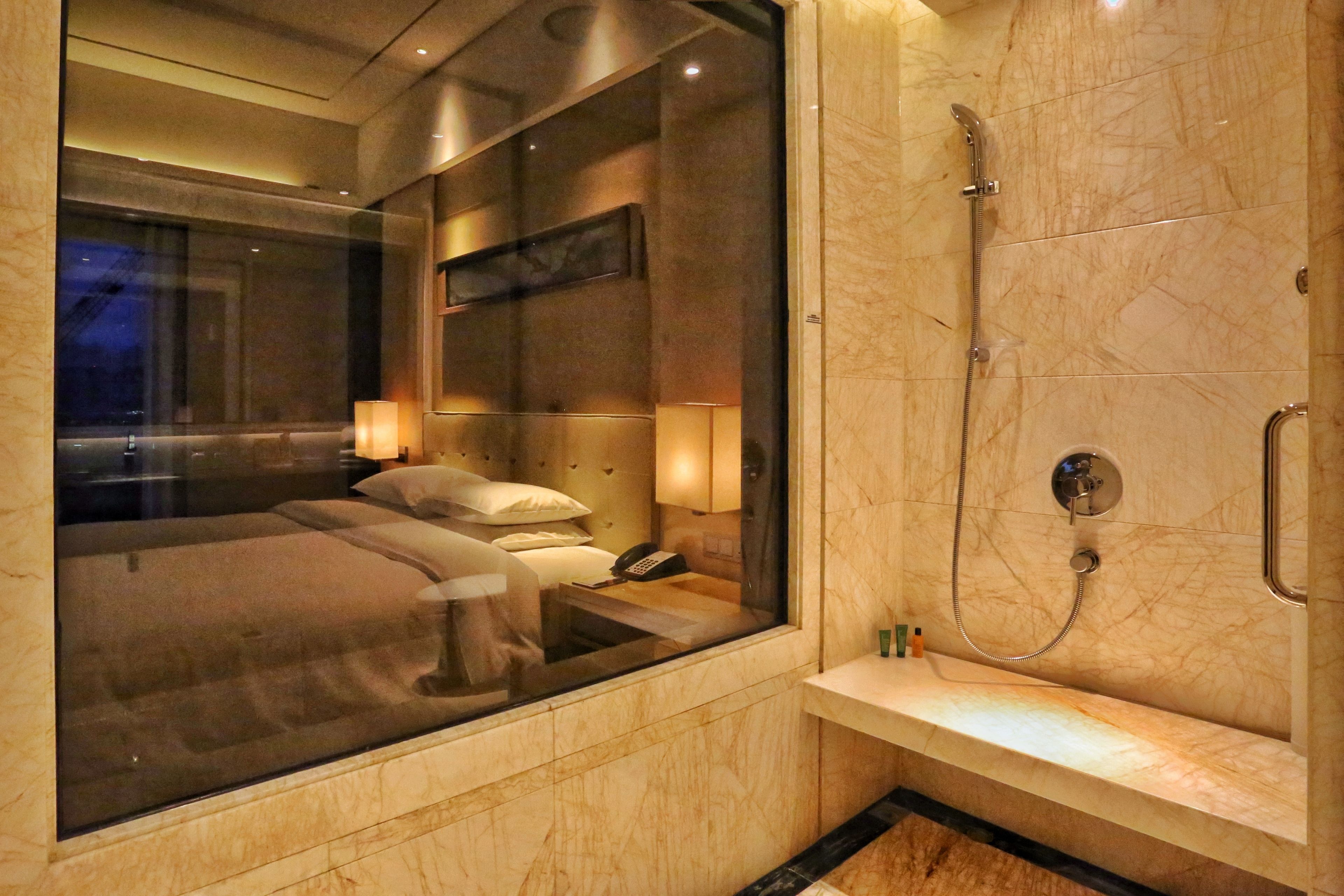 A modern hotel room with a large window, a shower area, and a bedside table.