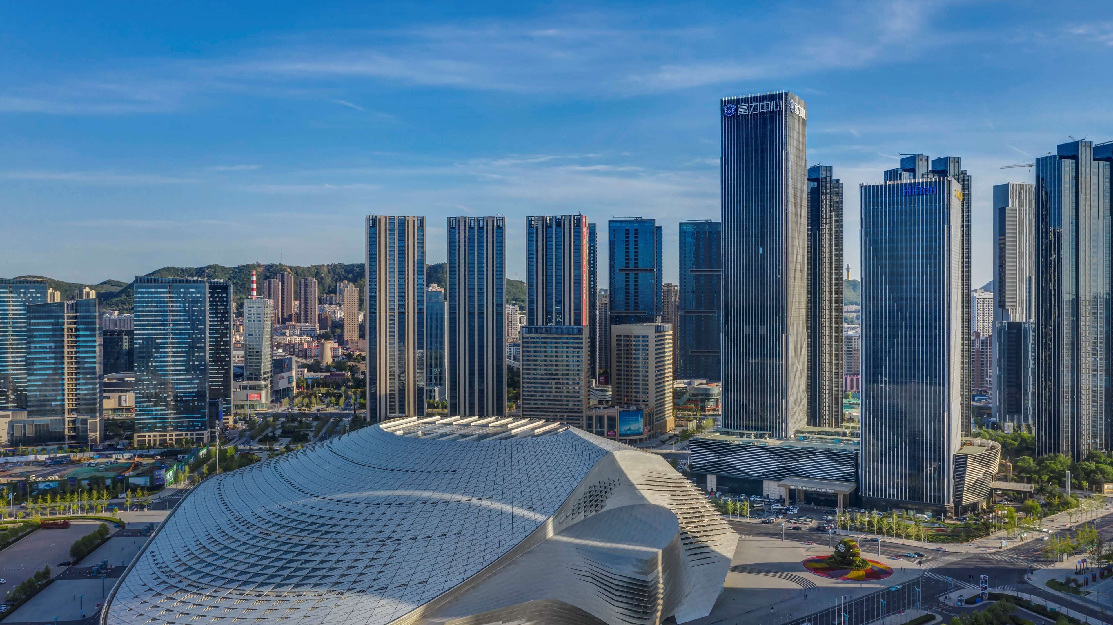 Un paisaje urbano moderno con edificios altos y una estructura arquitectónica distintiva con techo curvo.