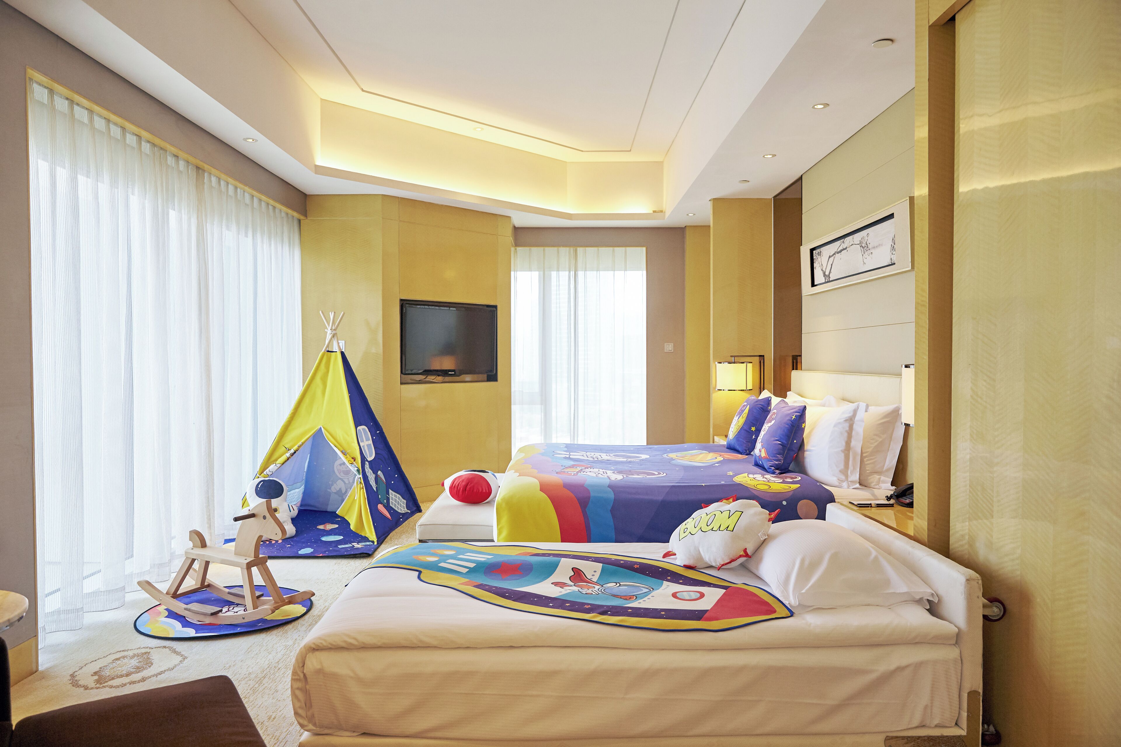 A hotel room with two beds, a tent, a rocking horse, and a flat-screen TV.
