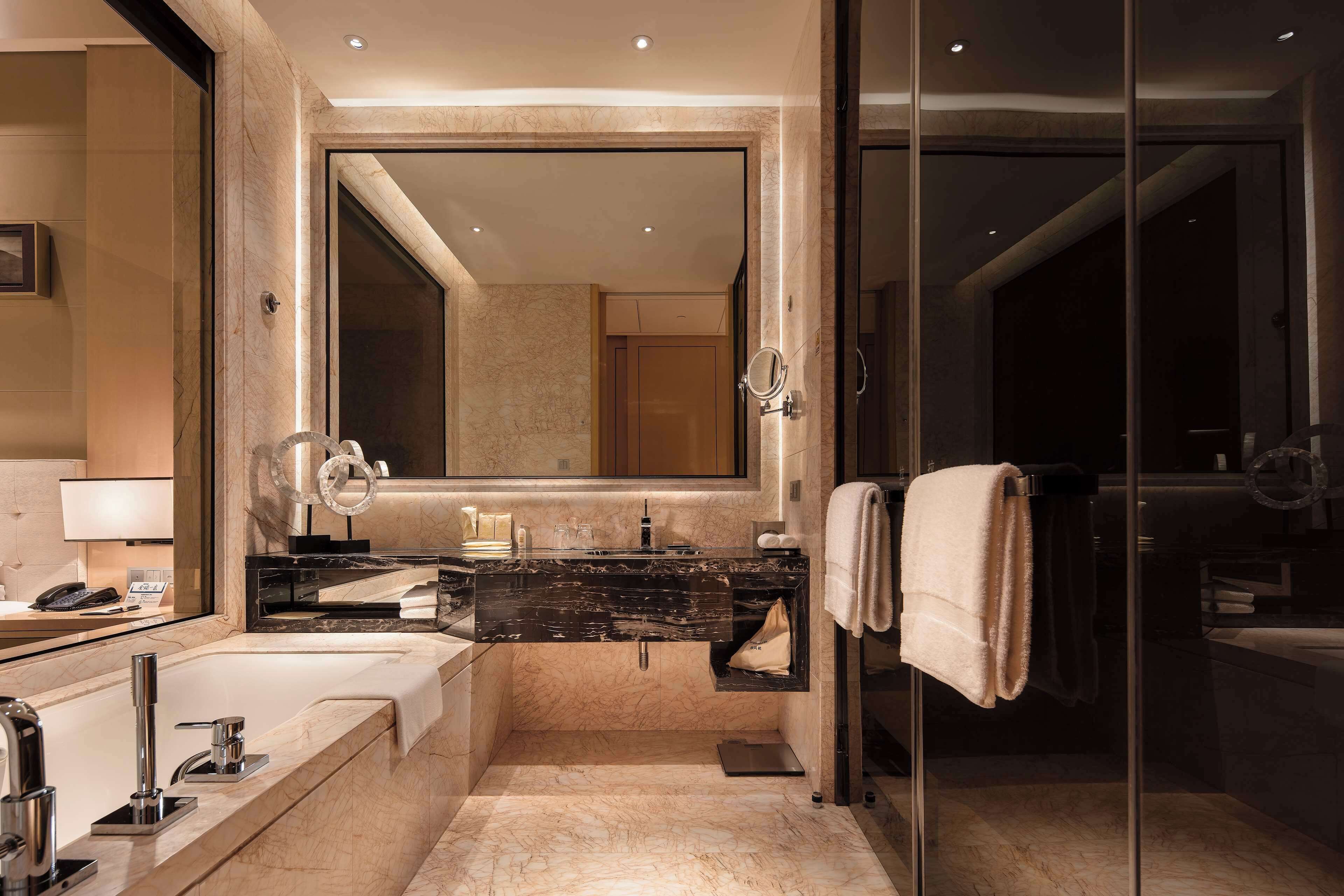 A modern bathroom with a large mirror, dual sinks, a glass shower enclosure, and a towel rack.