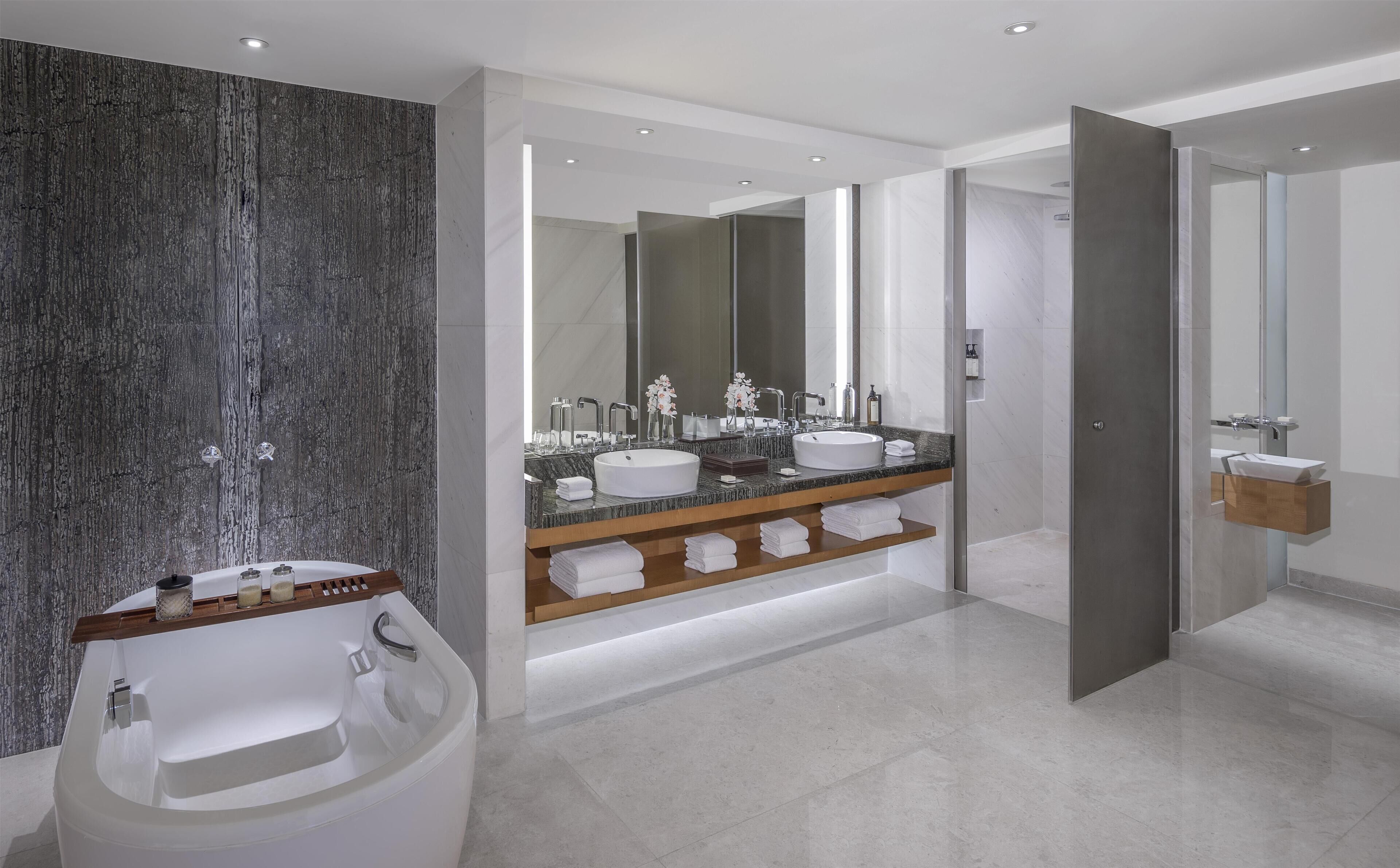 A modern bathroom with a large mirror, two sinks, a bathtub, and a shower area.