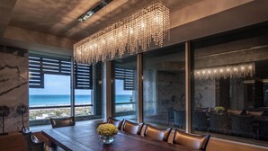 A dining area with a long table, chairs, a chandelier, and large windows with a view of the ocean. - Park Hyatt Abu Dhabi Hotel & Villas (Abu Dhabi)