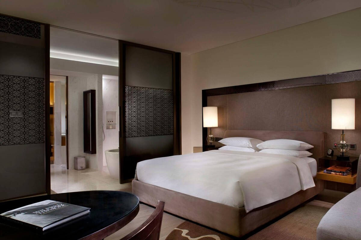 Une chambre d’hôtel avec un lit, des lampes de chevet, un bureau, une chaise et un grand miroir.