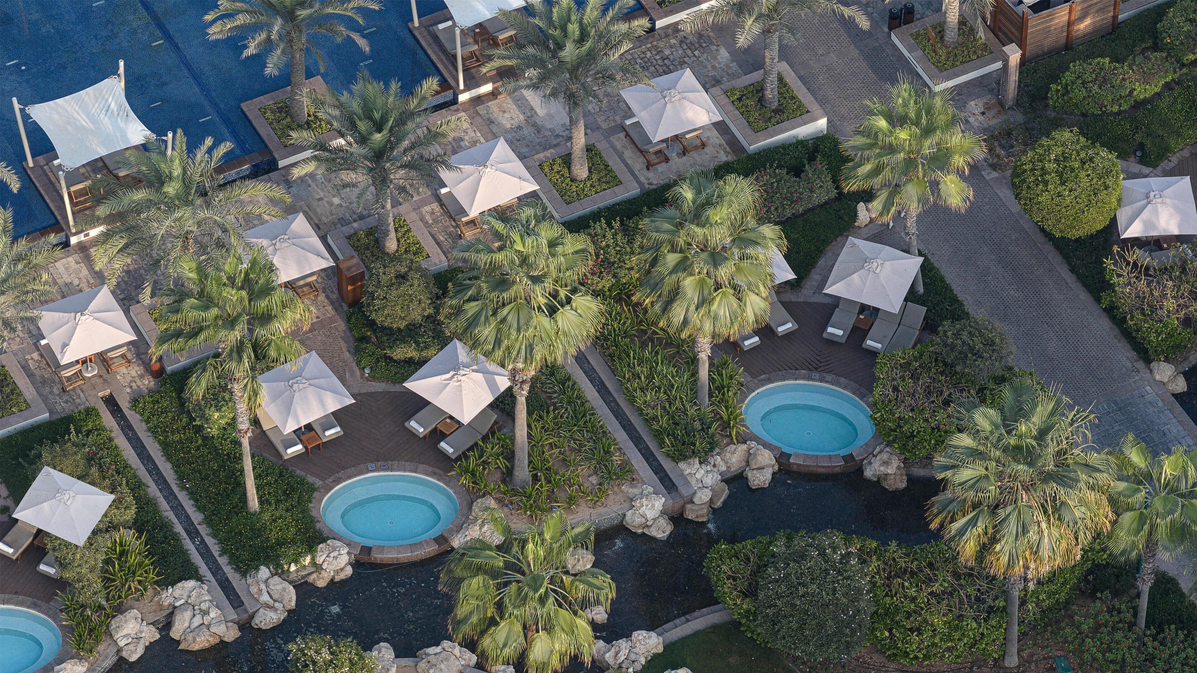 Vue aérienne d’un complexe hôtelier doté de plusieurs piscines, d’espaces de détente avec des parasols et de palmiers.