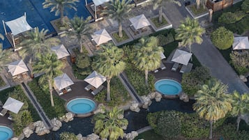 Vue aérienne d’un complexe hôtelier doté de plusieurs piscines, d’espaces de détente avec des parasols et de palmiers.