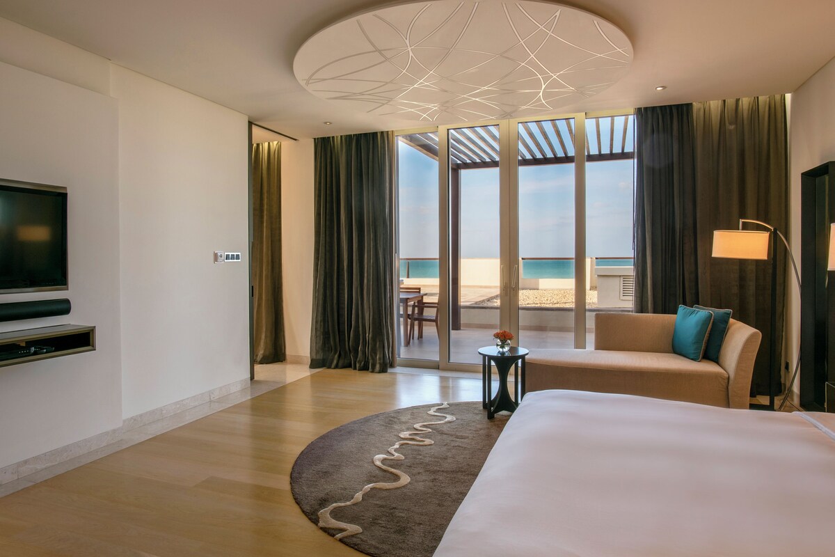 Une chambre d’hôtel avec un grand lit, un canapé, une télévision et vue sur la plage.