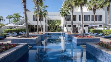 A pool area with tiled flooring, palm trees, and lounge chairs.