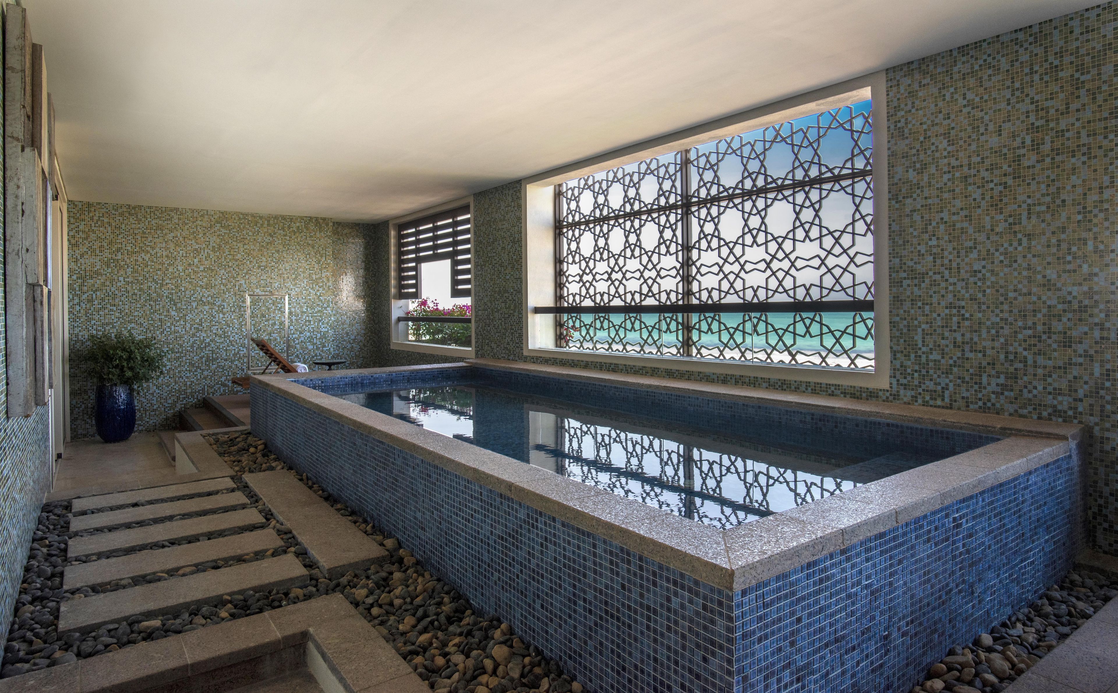 A swimming pool with a tiled border, a window with a lattice design, and a tiled wall with a pattern.