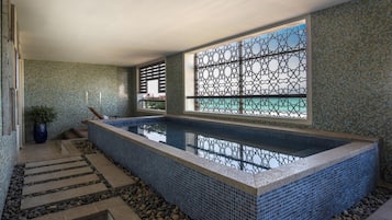 A swimming pool with a tiled border, a window with a lattice design, and a tiled wall with a pattern.