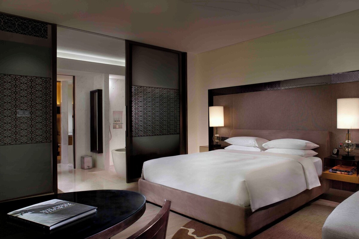 Une chambre d’hôtel comprenant un lit, des tables de chevet, une chaise, une petite table et un miroir.