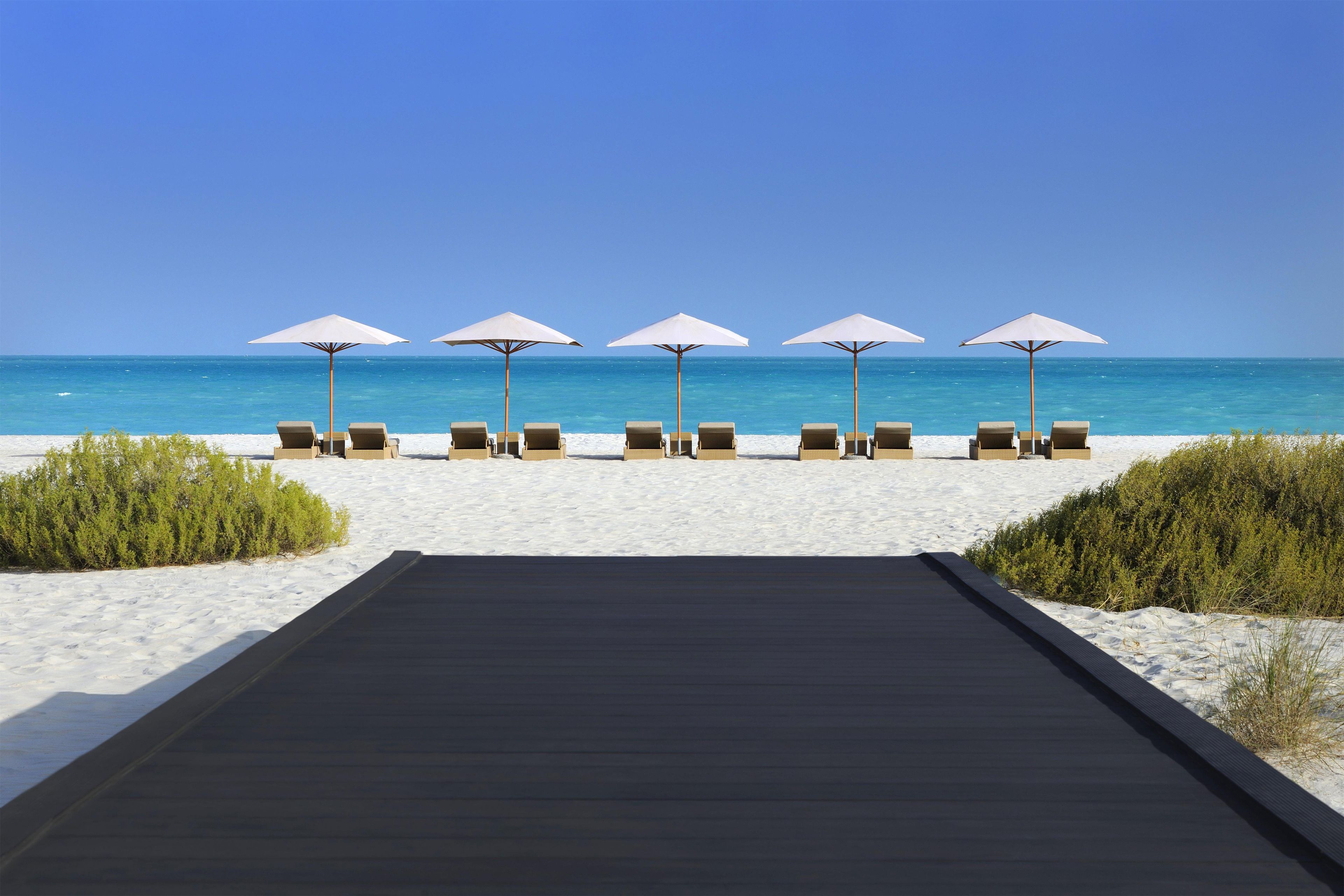 A beachside walkway leading to lounge chairs with umbrellas.