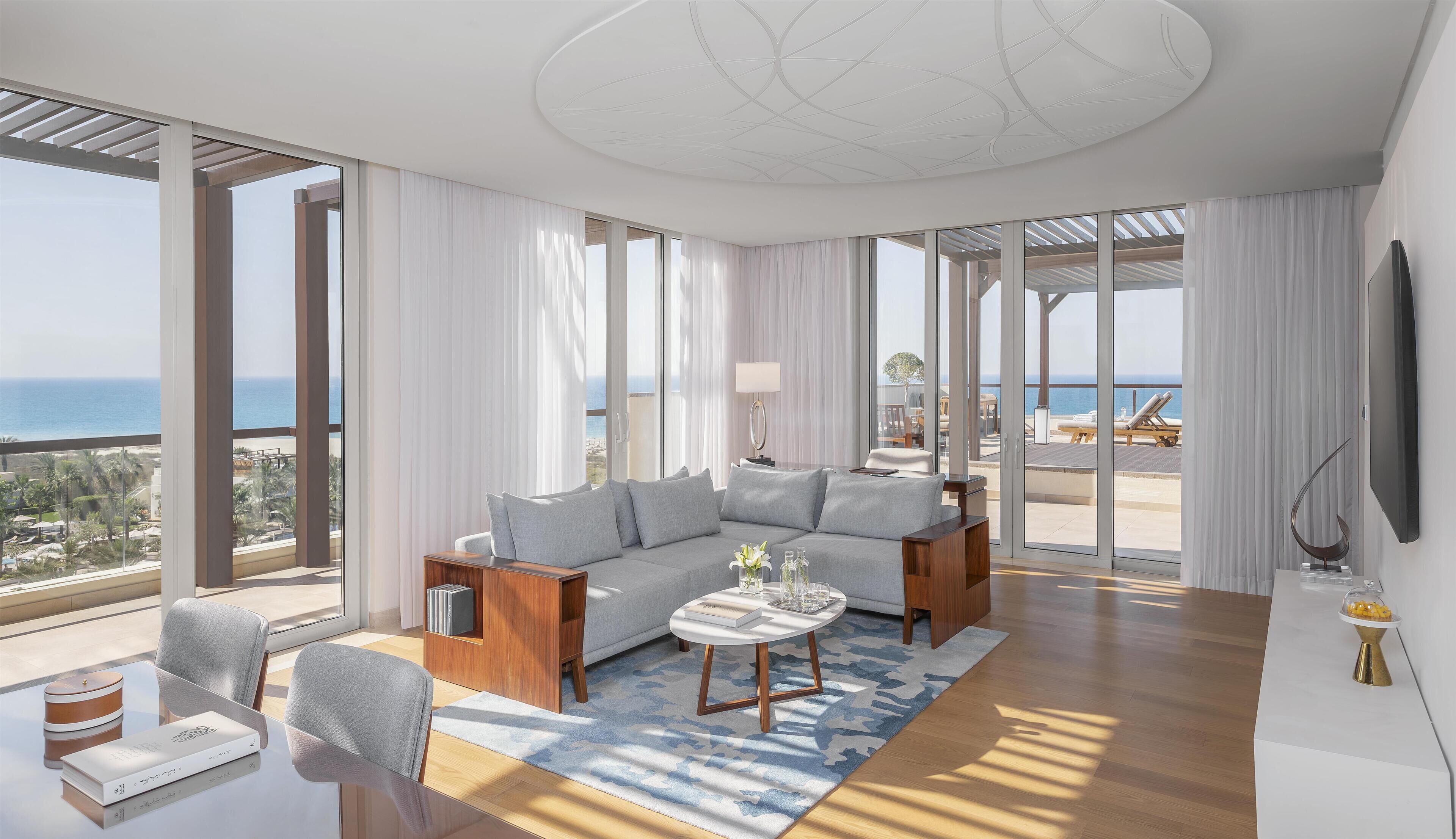 A modern living room with a large sofa, a coffee table, and a view of the sea.