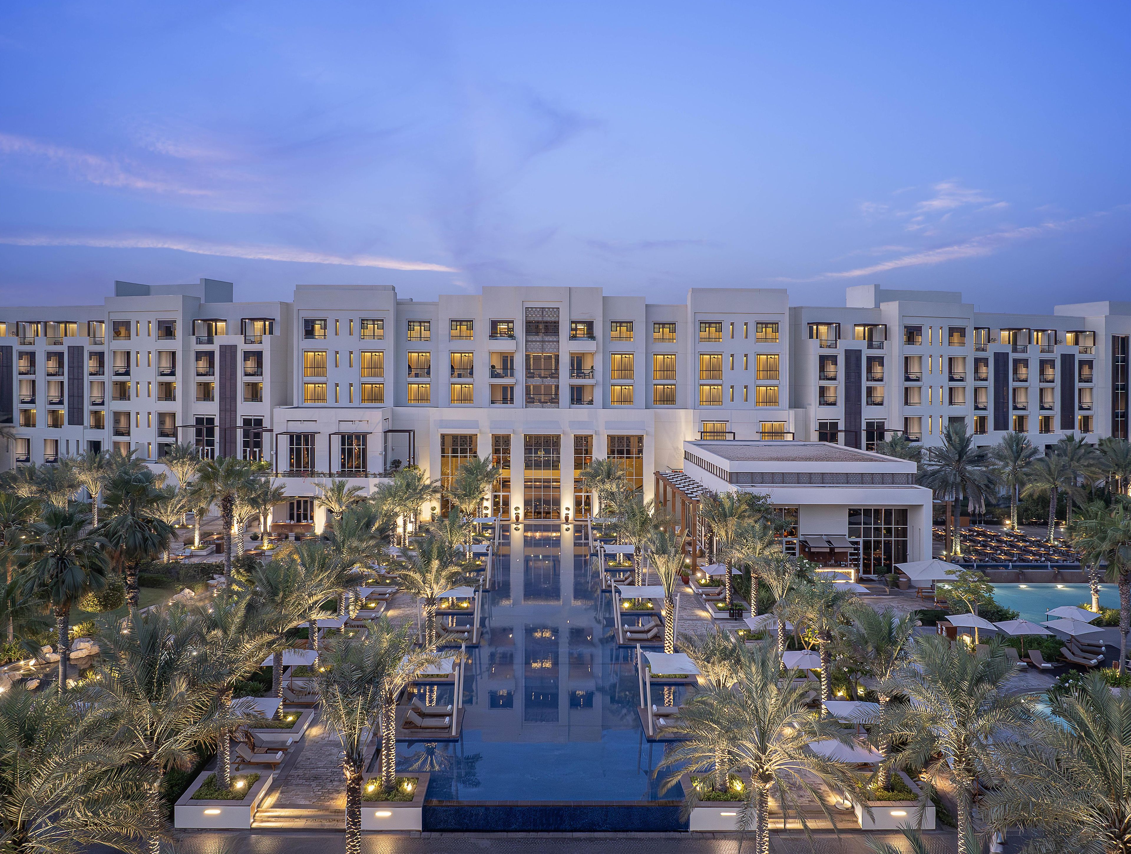 A hotel with multiple floors, a swimming pool, and palm trees.