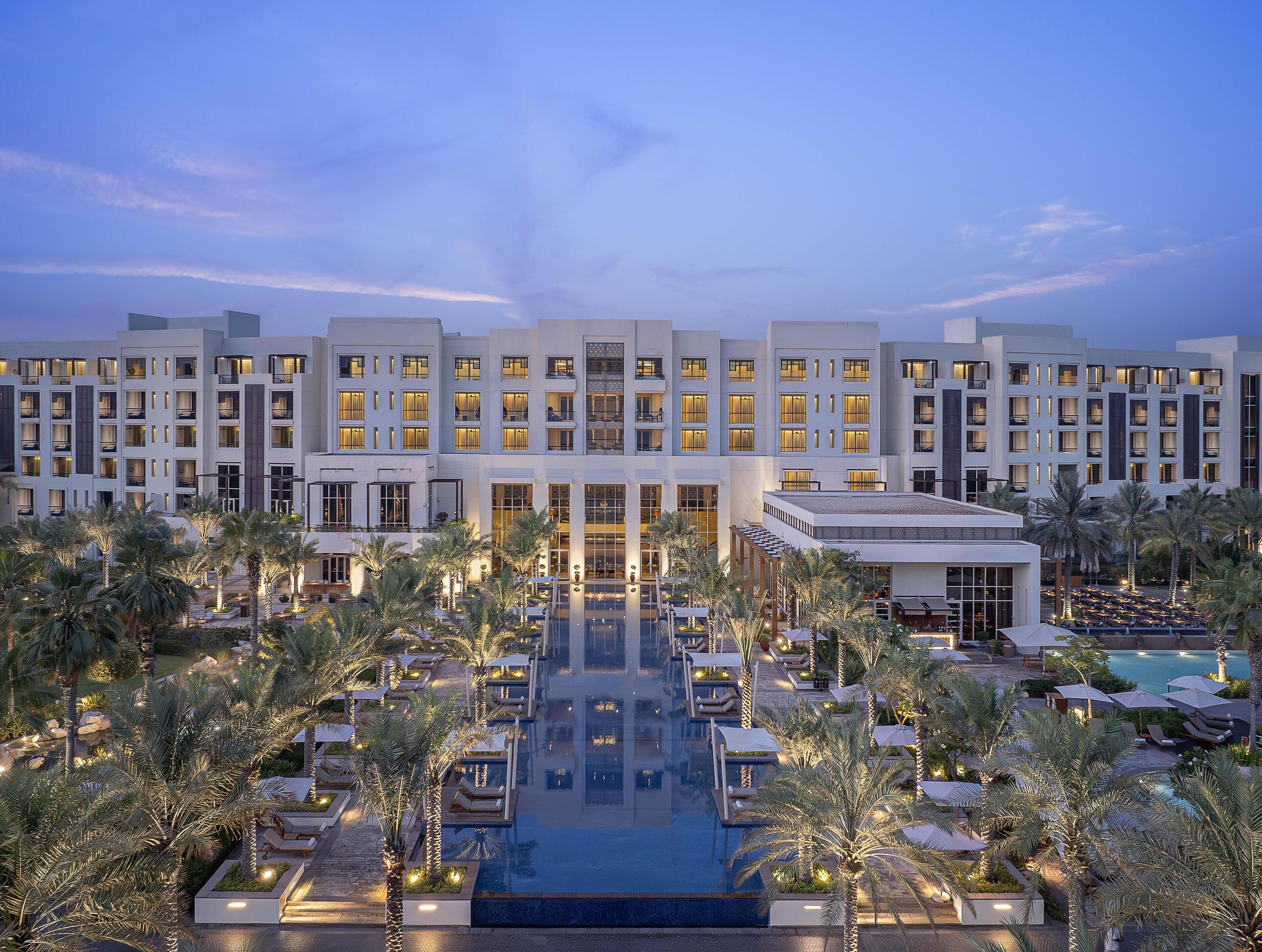 A hotel with multiple floors, a swimming pool, and palm trees.