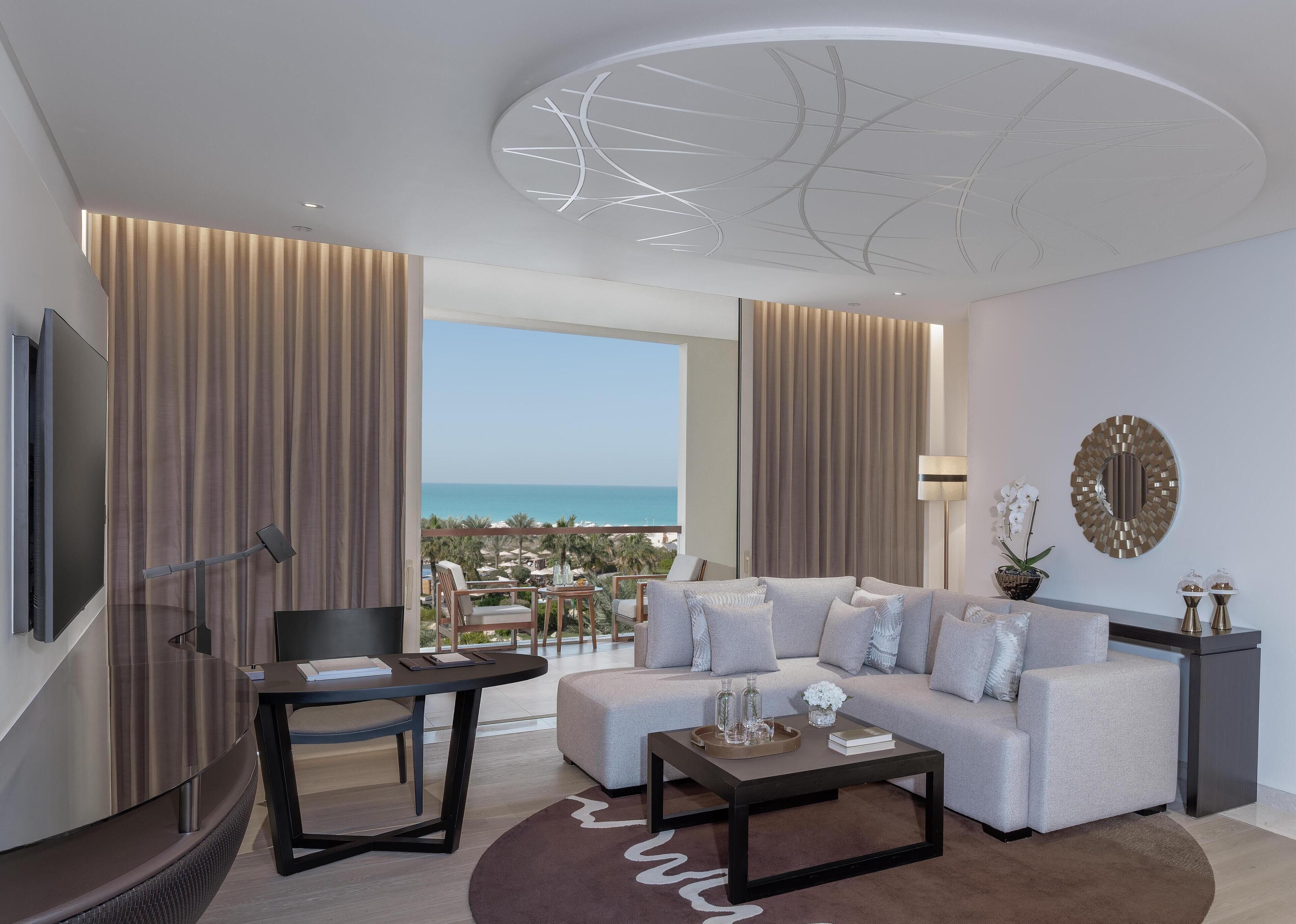 A modern living room with a sofa, coffee table, TV, and a balcony with a view of the sea.