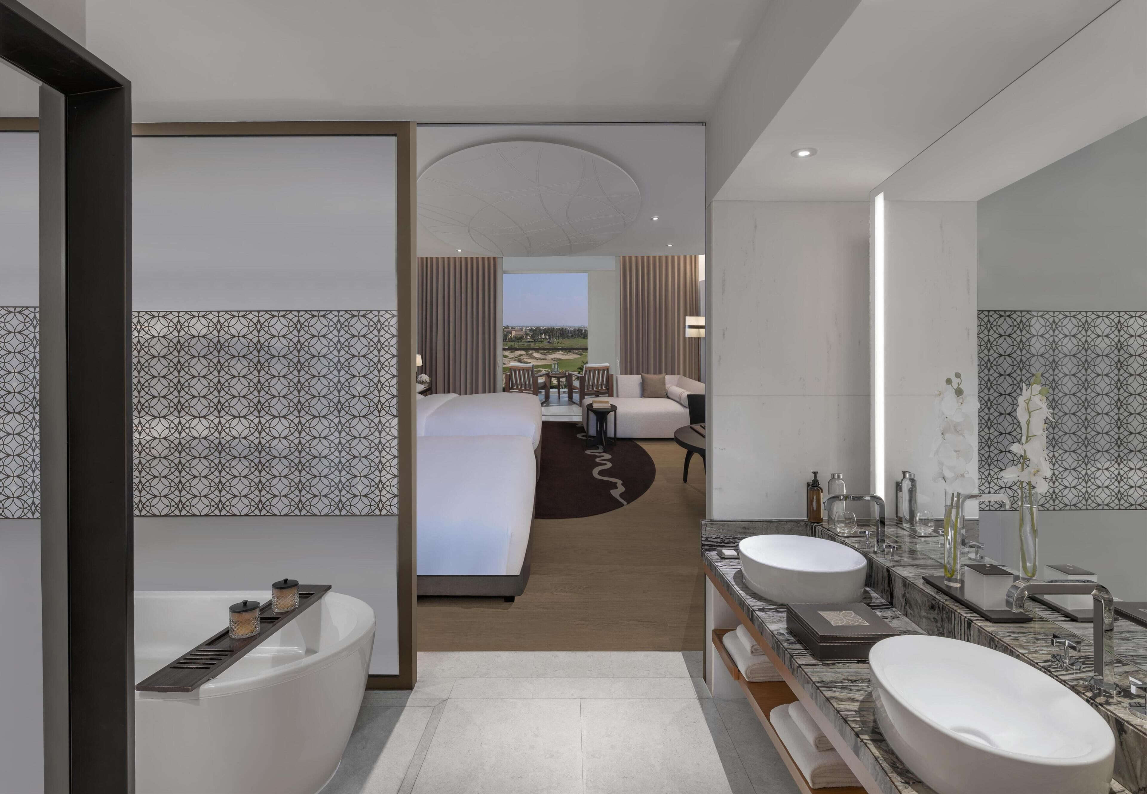 A modern hotel bathroom with a bathtub, two sinks, and a large mirror.