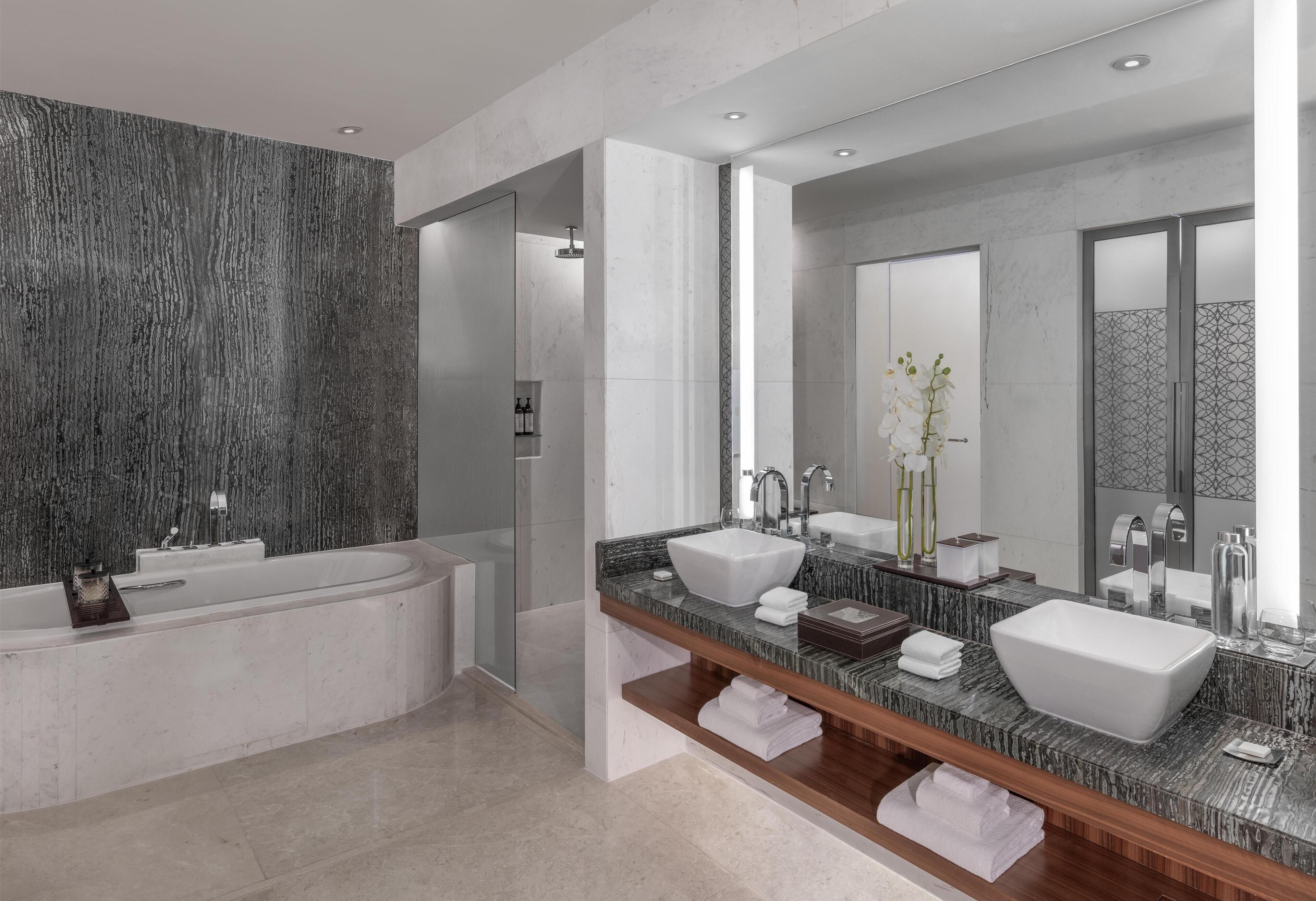 A modern bathroom with a freestanding bathtub, two sinks, a large mirror, and a marble countertop.