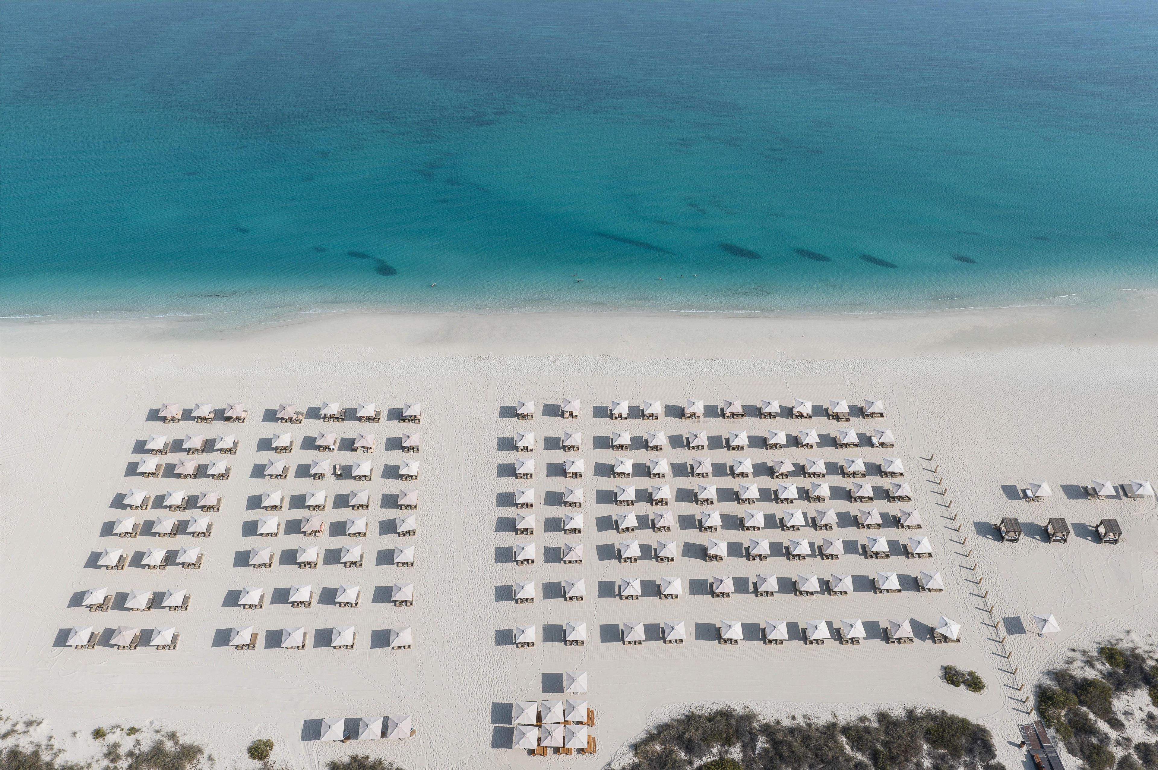 Une vue aérienne d’une plage où l’on aperçoit des rangées de tentes blanches et de parasols disposés en un motif quadrillé, avec l’océan en toile de fond.
