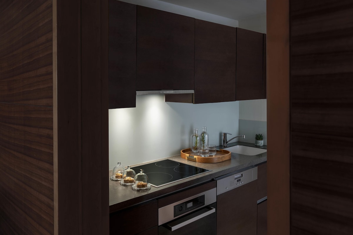 A modern kitchen with dark wood cabinets, a black stovetop, and a wooden tray with glass jars.